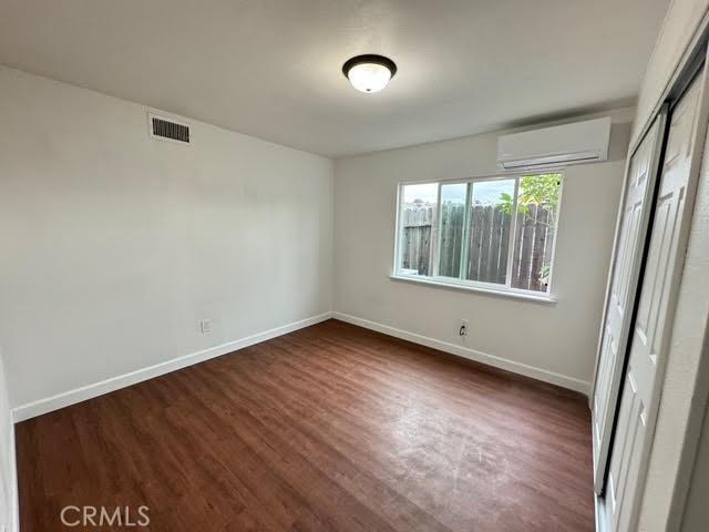 unfurnished bedroom featuring a wall mounted air conditioner, dark hardwood / wood-style flooring, and a closet