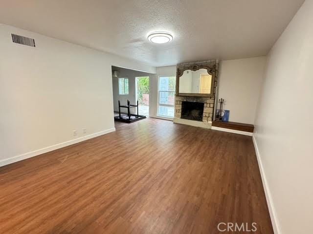 unfurnished living room featuring a stone fireplace, dark wood-type flooring, and a textured ceiling