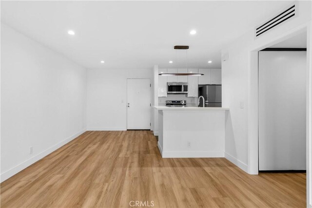 kitchen featuring light hardwood / wood-style floors, sink, hanging light fixtures, stainless steel appliances, and white cabinets