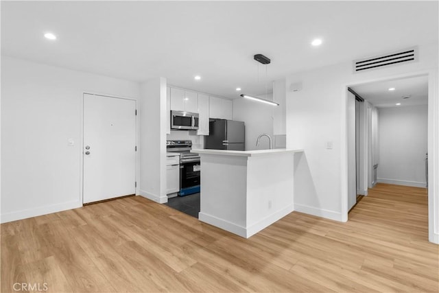 kitchen featuring kitchen peninsula, white cabinetry, hanging light fixtures, light wood-type flooring, and appliances with stainless steel finishes