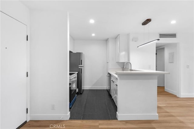 kitchen featuring pendant lighting, kitchen peninsula, sink, white cabinetry, and stainless steel appliances