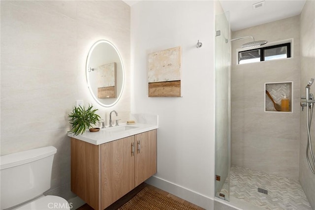 bathroom featuring toilet, tiled shower, and vanity