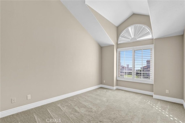 spare room featuring vaulted ceiling, carpet, and baseboards