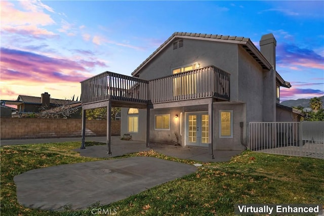 back house at dusk featuring a yard, a patio area, french doors, and a balcony