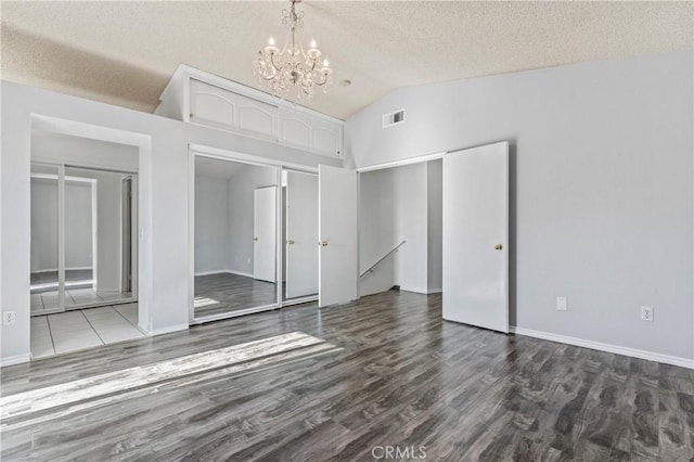 unfurnished bedroom featuring vaulted ceiling, an inviting chandelier, a textured ceiling, and hardwood / wood-style flooring