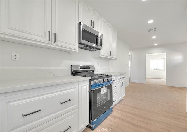 kitchen featuring light stone counters, white cabinetry, stainless steel appliances, and light wood-type flooring