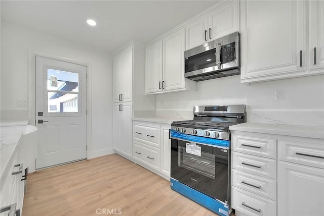 kitchen with stainless steel appliances, light hardwood / wood-style floors, white cabinetry, and light stone countertops