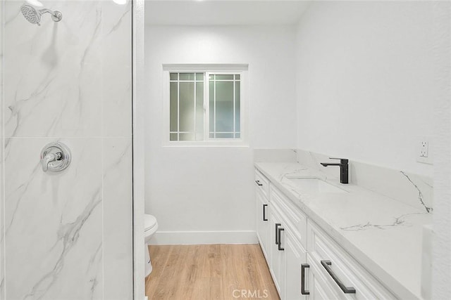 bathroom with toilet, a tile shower, hardwood / wood-style floors, and vanity