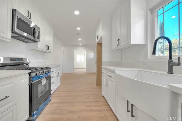 kitchen with sink, white cabinetry, light hardwood / wood-style flooring, appliances with stainless steel finishes, and light stone counters