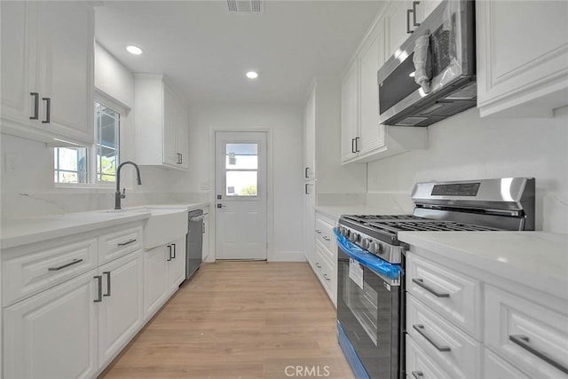 kitchen with stainless steel appliances, white cabinets, and light stone counters