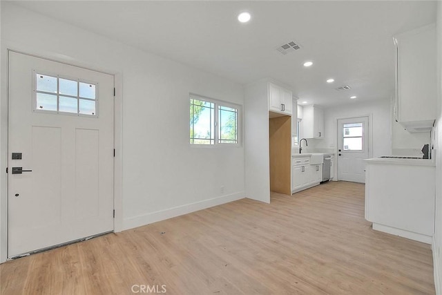 kitchen with stainless steel dishwasher, white cabinets, sink, and light hardwood / wood-style floors