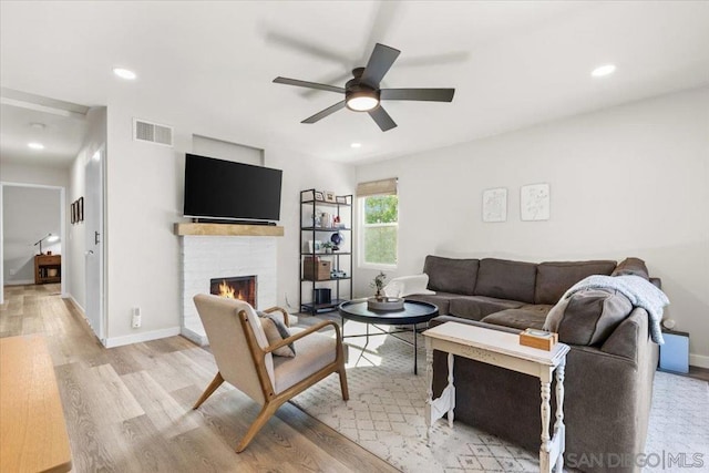 living room featuring light wood-type flooring, ceiling fan, and a tiled fireplace