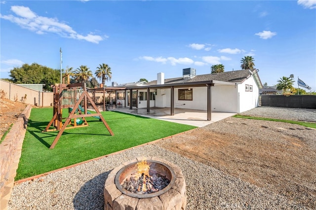 rear view of house with a playground, an outdoor fire pit, a patio, central AC, and a lawn