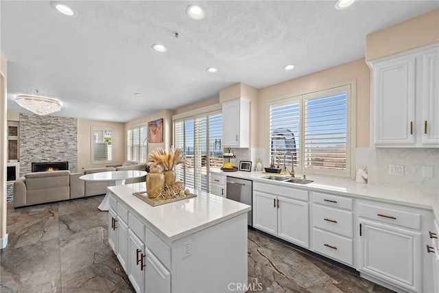 kitchen with a center island, white cabinetry, a fireplace, decorative backsplash, and sink