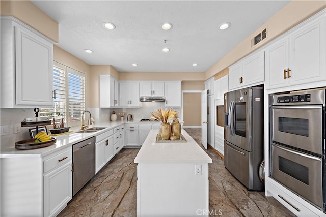 kitchen featuring white cabinets, appliances with stainless steel finishes, a kitchen island, sink, and backsplash