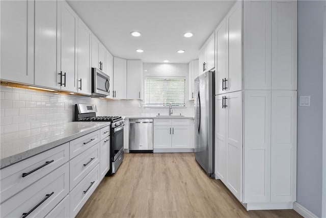 kitchen featuring appliances with stainless steel finishes, white cabinetry, light hardwood / wood-style floors, decorative backsplash, and light stone counters