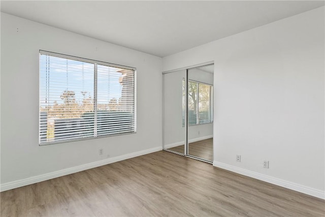 unfurnished bedroom featuring multiple windows, a closet, and light hardwood / wood-style flooring