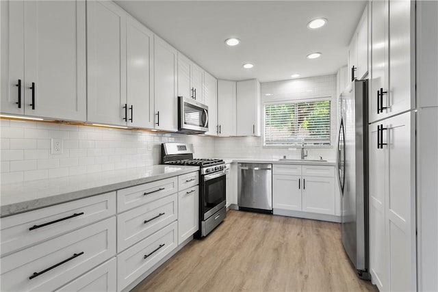 kitchen with appliances with stainless steel finishes, white cabinetry, tasteful backsplash, sink, and light stone counters