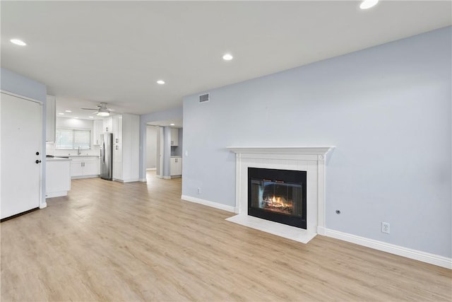 unfurnished living room featuring light hardwood / wood-style floors, a tile fireplace, and ceiling fan