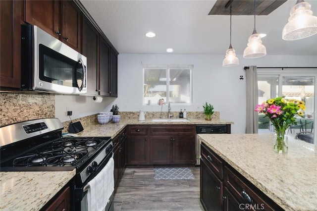 kitchen with appliances with stainless steel finishes, sink, dark brown cabinetry, light hardwood / wood-style flooring, and pendant lighting