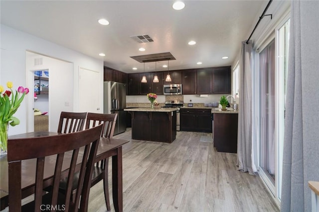 kitchen with dark brown cabinetry, appliances with stainless steel finishes, a kitchen island, decorative light fixtures, and light wood-type flooring