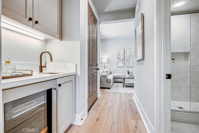 bar with wine cooler, a sink, light wood-style flooring, and baseboards