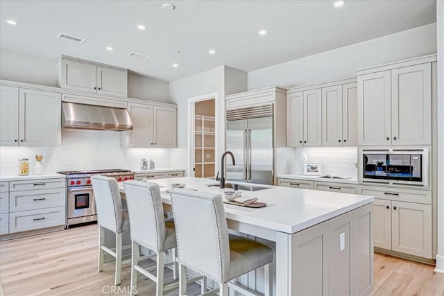 kitchen featuring built in appliances, light countertops, extractor fan, and a center island with sink