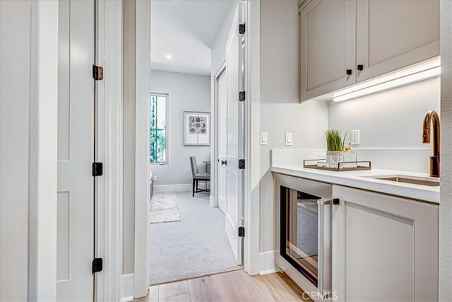 interior space featuring light colored carpet, light wood-style flooring, a sink, beverage cooler, and baseboards