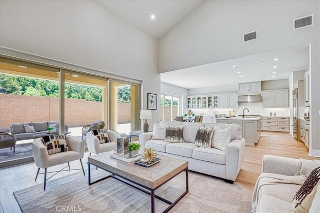 living room with high vaulted ceiling, sink, and light hardwood / wood-style floors