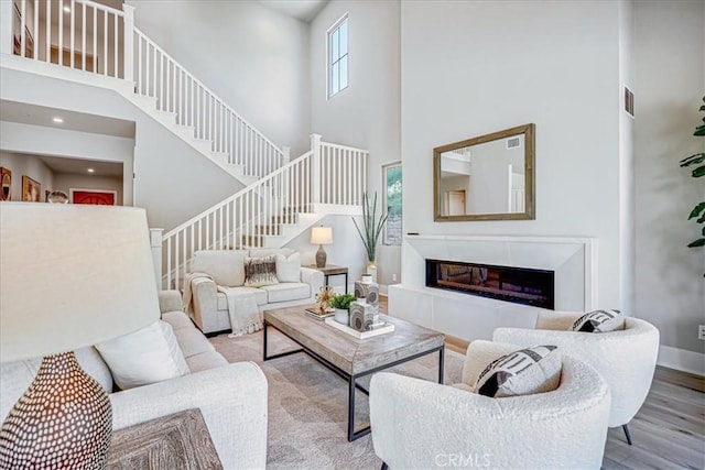 living area featuring a towering ceiling, baseboards, stairway, light wood-type flooring, and a glass covered fireplace