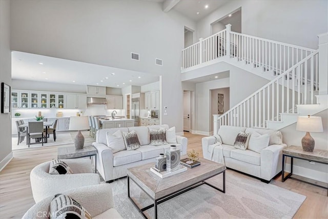 living room with a high ceiling, light hardwood / wood-style flooring, sink, and beamed ceiling