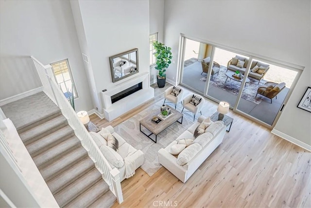 living area with a towering ceiling, light wood finished floors, a fireplace, and a wealth of natural light