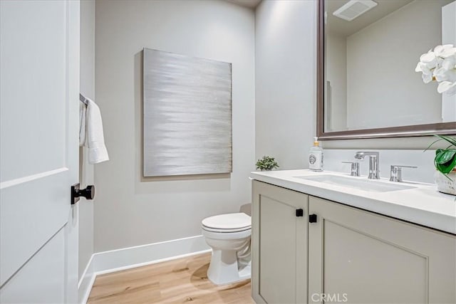 half bathroom with visible vents, toilet, vanity, wood finished floors, and baseboards