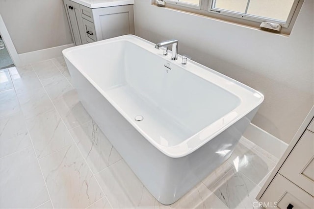 bathroom with marble finish floor, baseboards, and a soaking tub