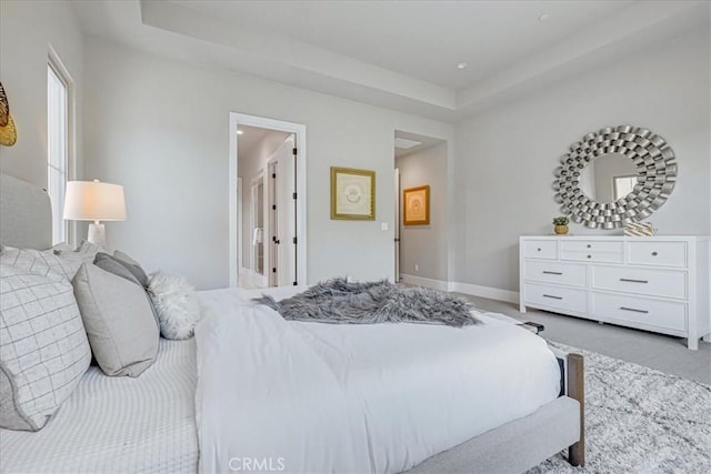 carpeted bedroom with a raised ceiling and baseboards