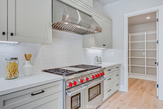 kitchen featuring tasteful backsplash, ventilation hood, range with two ovens, and white cabinetry