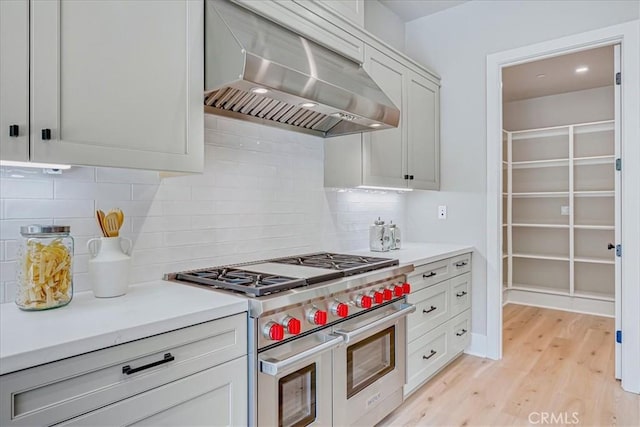 kitchen featuring white cabinets, double oven range, ventilation hood, and light countertops