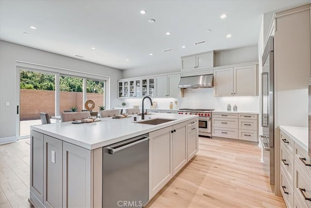 kitchen with light countertops, high end appliances, a center island with sink, and glass insert cabinets