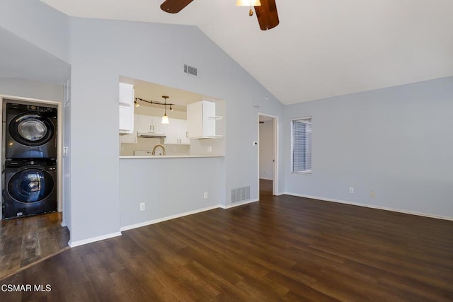 unfurnished living room featuring sink, dark hardwood / wood-style floors, stacked washer and clothes dryer, vaulted ceiling, and ceiling fan