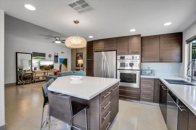 kitchen featuring sink, hanging light fixtures, dark brown cabinets, stainless steel appliances, and a center island