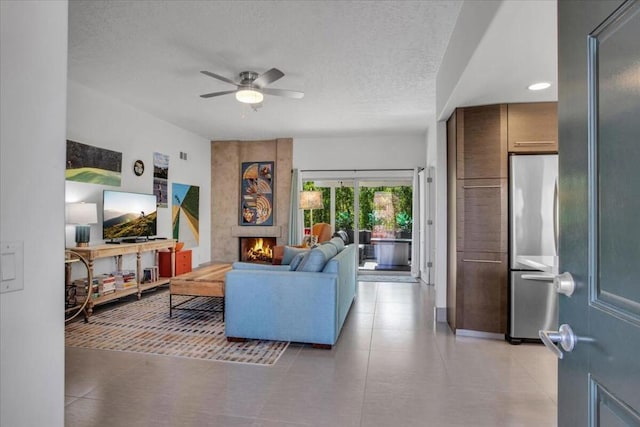 tiled living room featuring ceiling fan, a large fireplace, and a textured ceiling