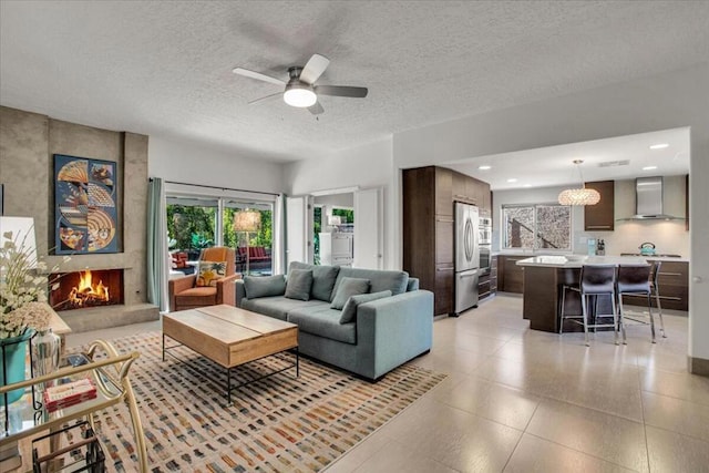 living room featuring ceiling fan, a large fireplace, and a textured ceiling