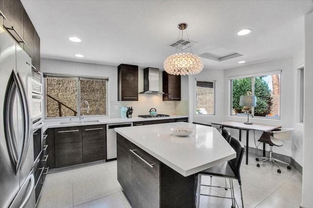 kitchen with appliances with stainless steel finishes, pendant lighting, sink, a center island, and wall chimney range hood