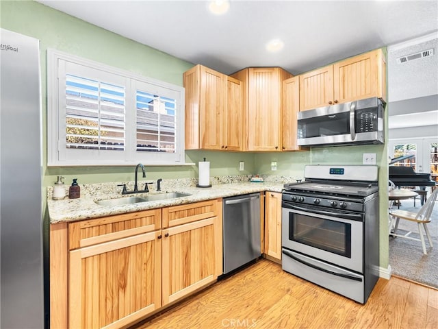 kitchen with appliances with stainless steel finishes, sink, light brown cabinetry, and light wood-type flooring