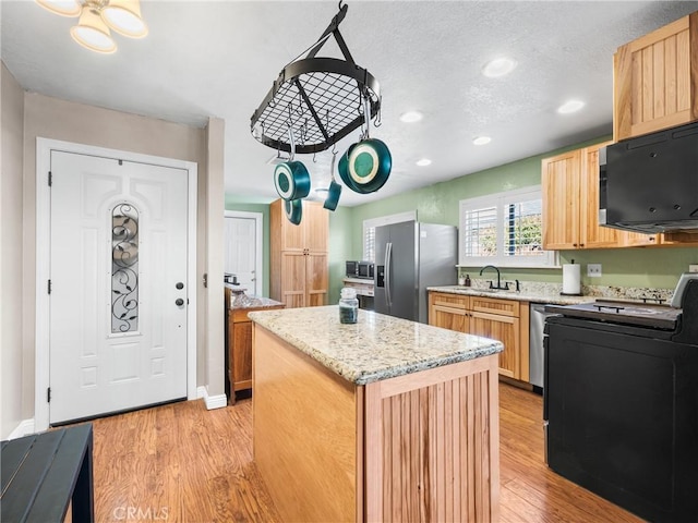 kitchen with a kitchen island, appliances with stainless steel finishes, light brown cabinetry, sink, and light hardwood / wood-style floors