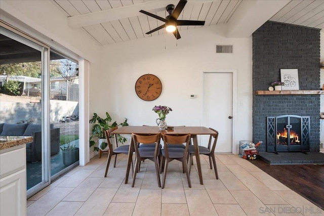 dining room with vaulted ceiling with beams, light tile patterned floors, ceiling fan, a brick fireplace, and wooden ceiling