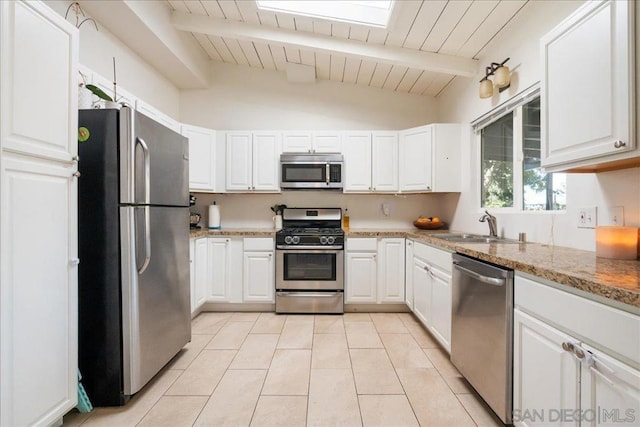 kitchen featuring white cabinetry, appliances with stainless steel finishes, lofted ceiling with skylight, and light stone countertops