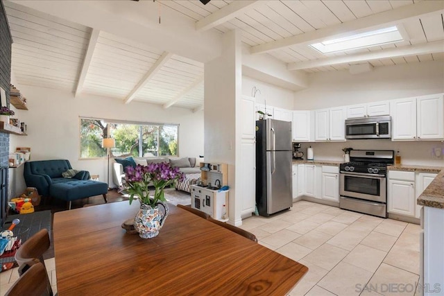 kitchen featuring light tile patterned floors, appliances with stainless steel finishes, beamed ceiling, dark stone counters, and white cabinets