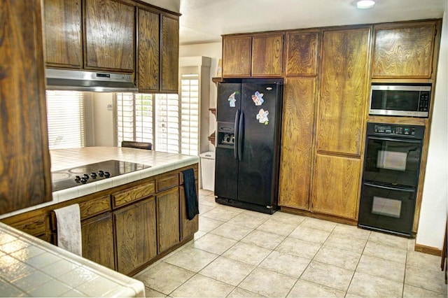 kitchen with light tile patterned floors, tile counters, and black appliances