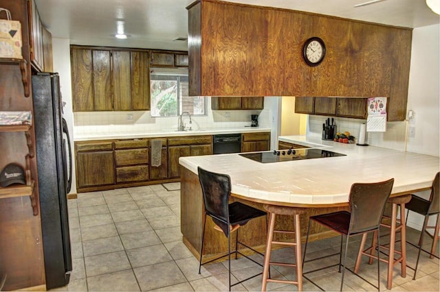 kitchen featuring light tile patterned flooring, kitchen peninsula, tasteful backsplash, a breakfast bar area, and black appliances